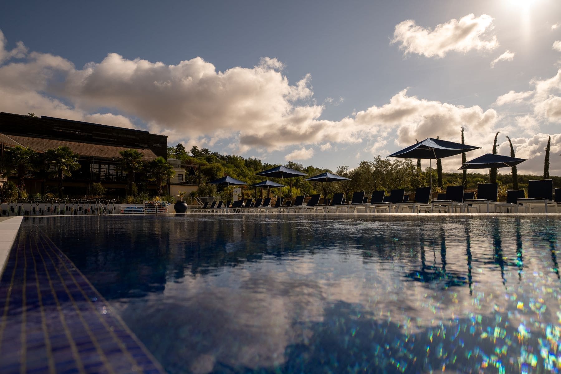 Piscine extérieure du country club, transats et parasols sous un ciel de fin de journée