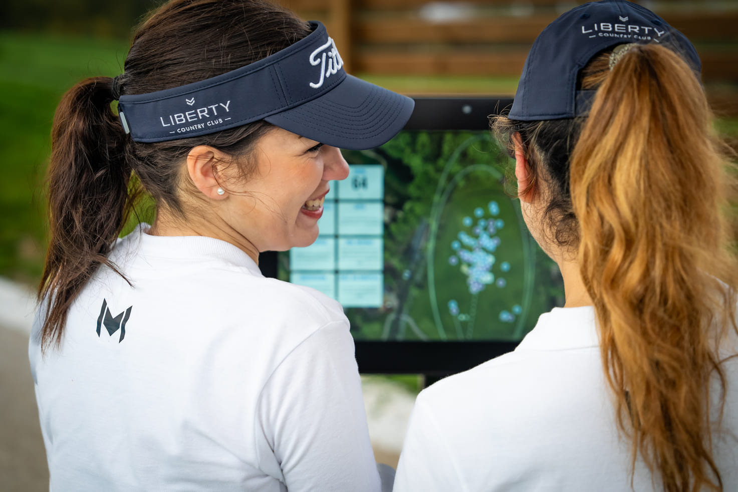 Deux golfeuses en casquette Liberty Country Club observent les données de leur swing sur l'écran du practice Trackman